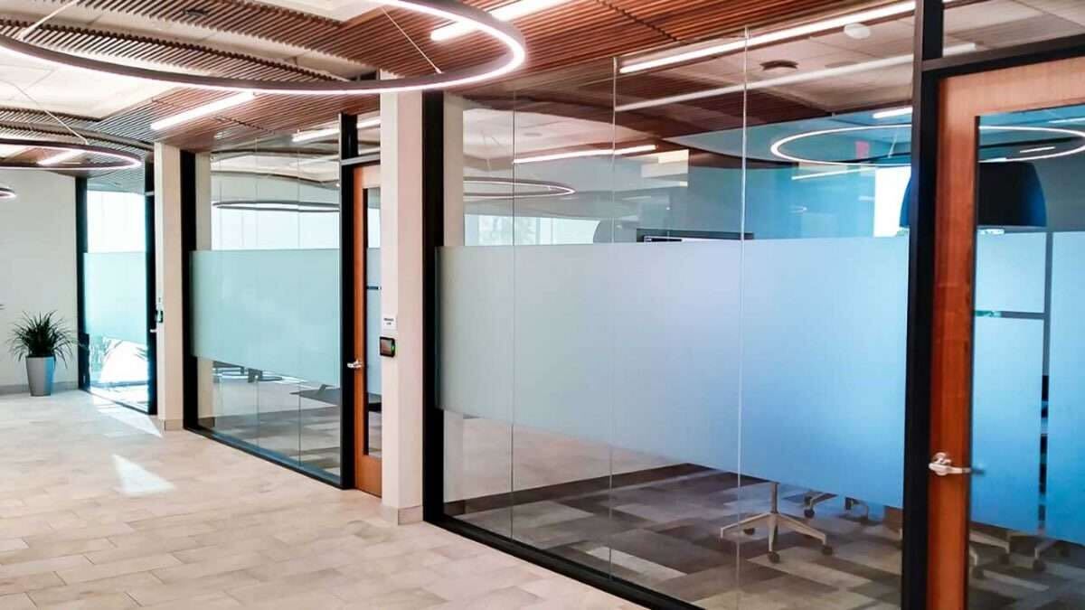 Black sedan parked by a glass building with trees and hills in the background.